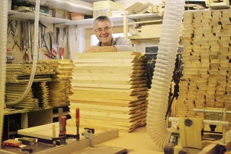 Team von Mypaketkasten produziert Rhomuslatten in hauseigener Werkastatt. Aufgestapelte Holzleisten stehen auf Werkbank. Werkzeuge hängen an der Wand.