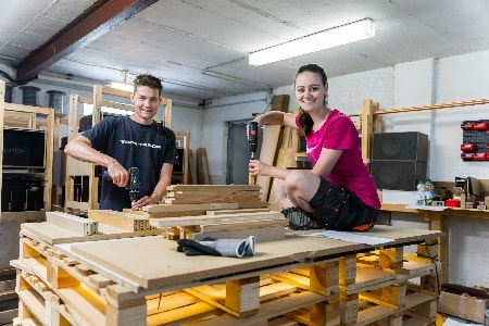 Das Team von Mypaketkasten arbeitet in der Gründerwerkstatt. Aufeinander gestapelte Paletten dienen als Arbeitstisch.